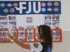 a woman holding a remote in front of a wall with pictures on it