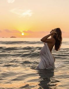 a woman standing in the ocean at sunset with her hands on her head and eyes closed