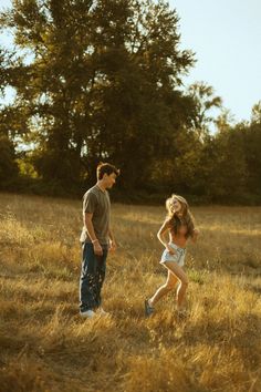 a man and woman are walking through the tall grass with trees in the back ground