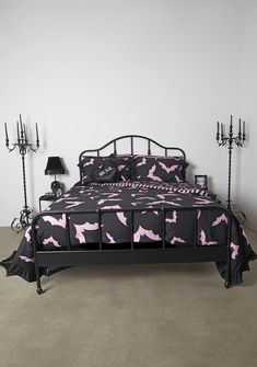 a bed with pink and black bedspread in a bedroom next to two candelabras