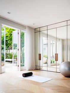 a yoga mat sits on the floor in front of mirrored walls and doors, with an exercise ball next to it