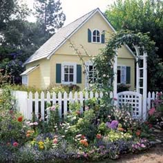 a yellow house surrounded by flowers and greenery