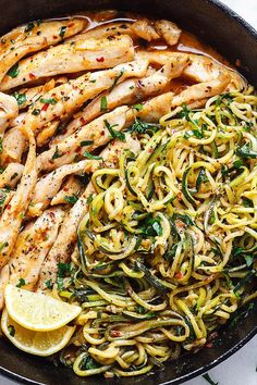 a skillet filled with pasta, chicken and lemon wedges on top of a table