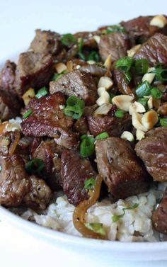 a white plate topped with meat and rice covered in green onion garnishments