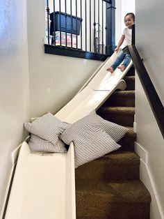 a little boy is sliding down the stairs with a slide in his hand and pillows on the floor