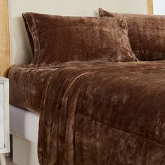 a bed with brown comforter and pillows on it's side table next to a window