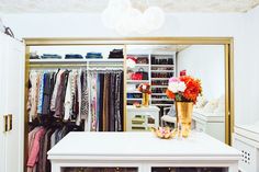 an organized closet with clothes, shoes and flowers on the top shelf in front of it