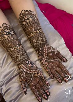 two hands with henna tattoos on them sitting on top of a white bed next to each other