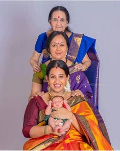 three women and one baby are posing for a family photo in their colorful sari outfits