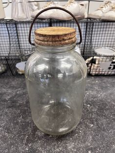 a glass jar with a cork lid on the floor next to other containers and baskets