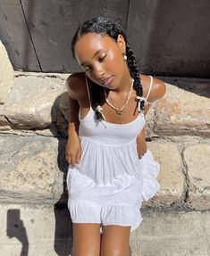 a woman in white dress leaning against stone wall