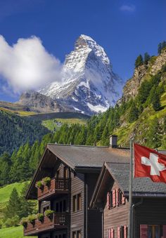 a swiss flag flying in front of a house with a mountain in the background,