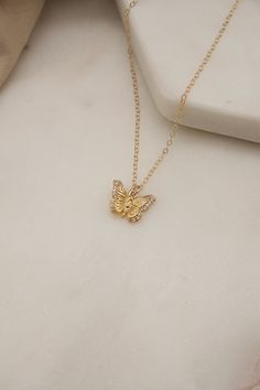 a gold necklace with a small butterfly on it's side, sitting on a white surface