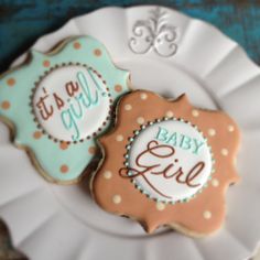 two decorated cookies sitting on top of a white plate next to each other with the words happy