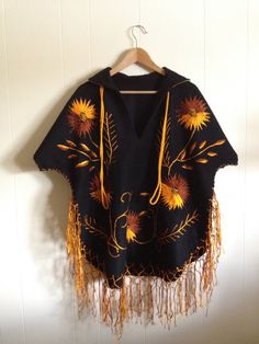 "Mexican folk embroidered poncho / cape / serape. Stunning. Deep black wool with vivid gold and copper embroidery. Collar with gold fabric beneath. Detailed embroidery on front and back. Beautiful hem fringe and long, gold cord at neck The condition is clean and rustic. No holes, wear or split seams. There are a few, expected pulls in the vintage embroidery hand work. Approximate Measurements: No tags. Underarm to underarm-29\" Sleeve length- 15\" - Short sleeve measured from hem of sleeve to ed Embroidered Long Sleeve Poncho For Festival, Winter Festival Embroidered Poncho, Traditional Long Sleeve Embroidered Poncho, Winter Embroidered Long Sleeve Poncho, Traditional Embroidered Poncho For Winter, Traditional Embroidered Winter Poncho, Black Cape For Fall Festivals, Black Fall Festival Cape, Traditional Fall Poncho With Fringe