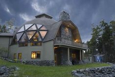 a large house with a glass roof and stone walls on the front lawn at night