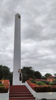 a tall white monument with steps leading up to it and flowers in the foreground