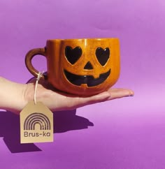 a hand holding a coffee mug with a carved pumpkin face on it's side