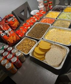 a table filled with lots of food on top of metal trays next to cans of soda