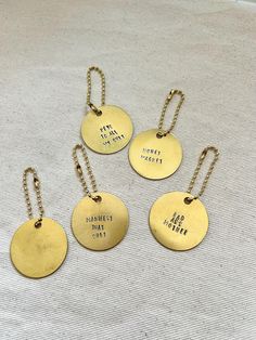 five gold tags with words on them sitting on a white cloth covered surface, one has a metal chain and the other has a small round tag that says do not