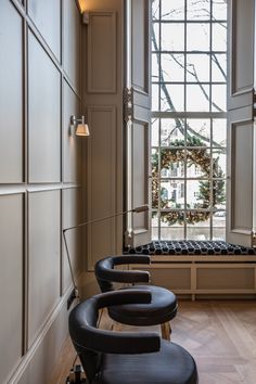 two black chairs sitting in front of a window with a wreath on the wall behind them