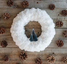 a snow covered wreath with pine cones and small trees in the middle on a wooden table