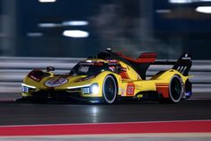 a yellow race car driving on a track at night time with motion blurry in the background