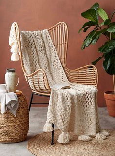 a wicker chair with a white crocheted blanket on it next to a potted plant