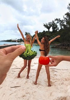 two women in bikinis on the beach holding up fruits and vegetables with their hands