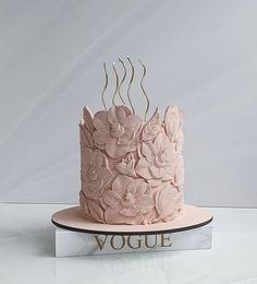 there is a pink cake with flowers on it and the word voge written in gold