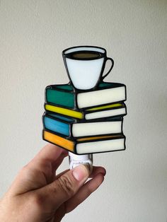 a hand holding up a small stained glass coffee cup on top of a stack of books