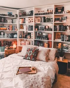 a bed with white sheets and pillows in front of bookshelves filled with books