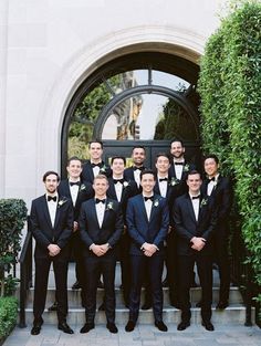 a group of men standing next to each other in front of a door wearing tuxedos