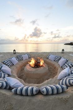 a fire pit on the beach with pillows around it