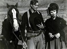 an old black and white photo of two men standing next to a horse in the desert