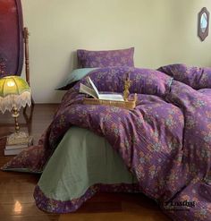 a bed with purple and green comforters in a room next to a lamp on a wooden floor