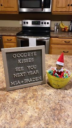 an elf is sitting next to a sign that says goodbye kisses see you next year mia - brady