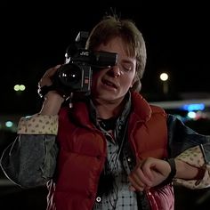 a man holding a camera up to his face in front of a car at night