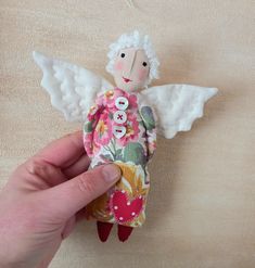 a hand holding a small doll with white wings and flowers on it's body