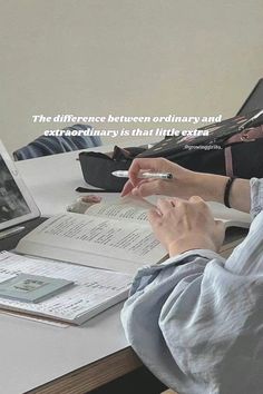 a woman sitting at a desk with a book and laptop in front of her, reading the bible