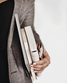 a woman holding two books and a ring on her left hand while wearing a gray blazer