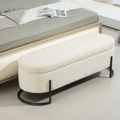 a white bench sitting on top of a floor next to a bed with a magazine