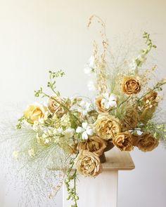 an arrangement of flowers in a vase sitting on a table next to a white wall