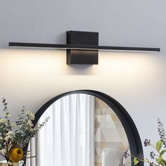 a round mirror sitting on top of a wall next to a vase with flowers in it