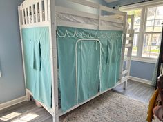 a bunk bed with blue sheets and curtains on the bottom level, in a room with hardwood flooring