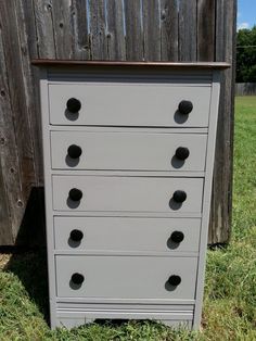 a gray dresser sitting in the grass next to a wooden fence