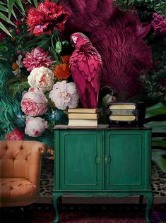 a parrot sitting on top of a green cabinet next to a flower filled wallpaper