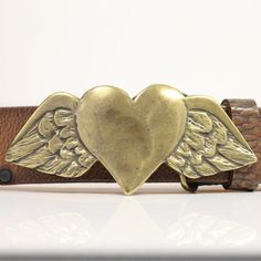 a gold heart with wings on a brown leather belt that is sitting on a white surface