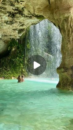 people are swimming in the water near a cave with a waterfall and rocks on either side