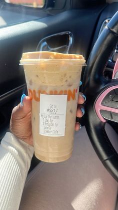 a woman holding up a cup of coffee in her car